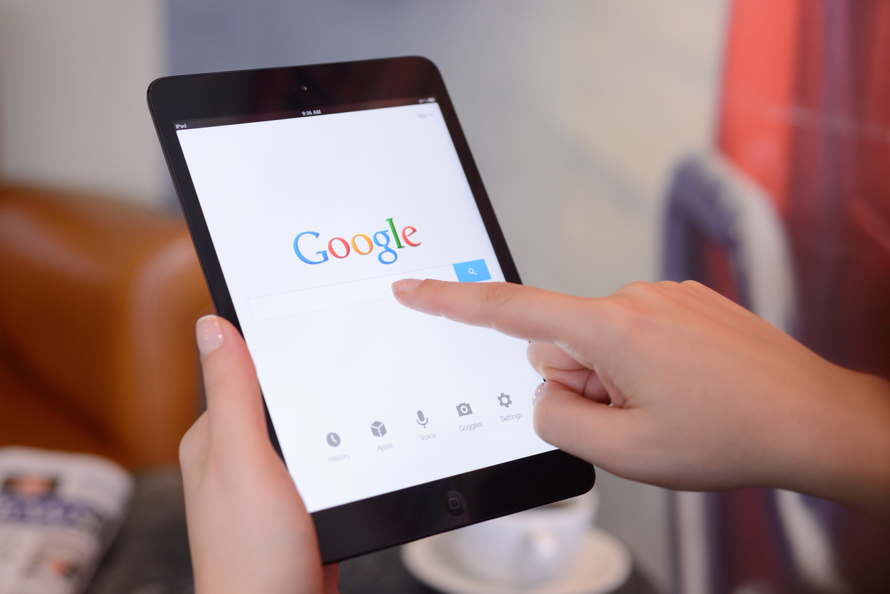 Hands holding an iPad Mini which displays the Google search homepage
